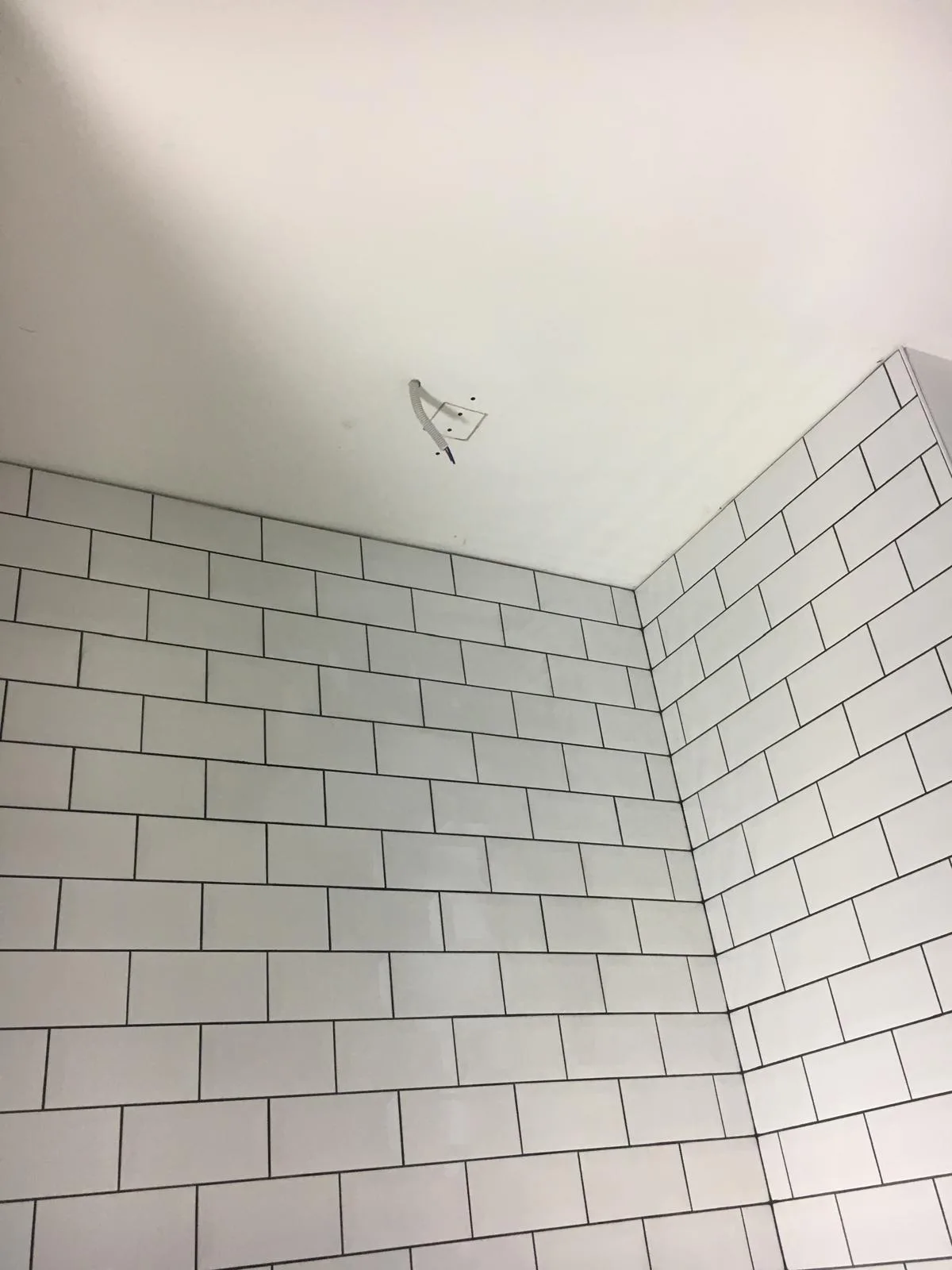 Hoek van een badkamer met witte tegels en een onvoltooid plafond