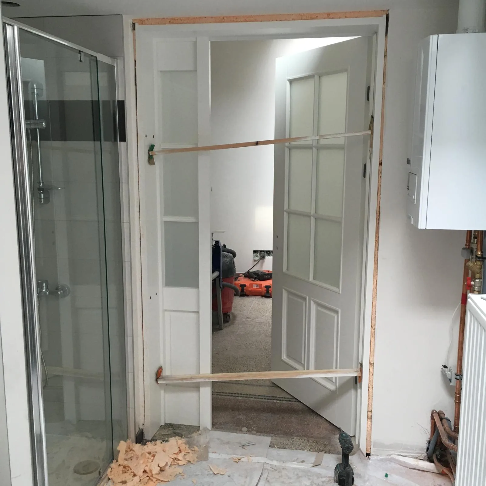 Deur in verbouwing met hout in de opening en renovatiemateriaal op de vloer