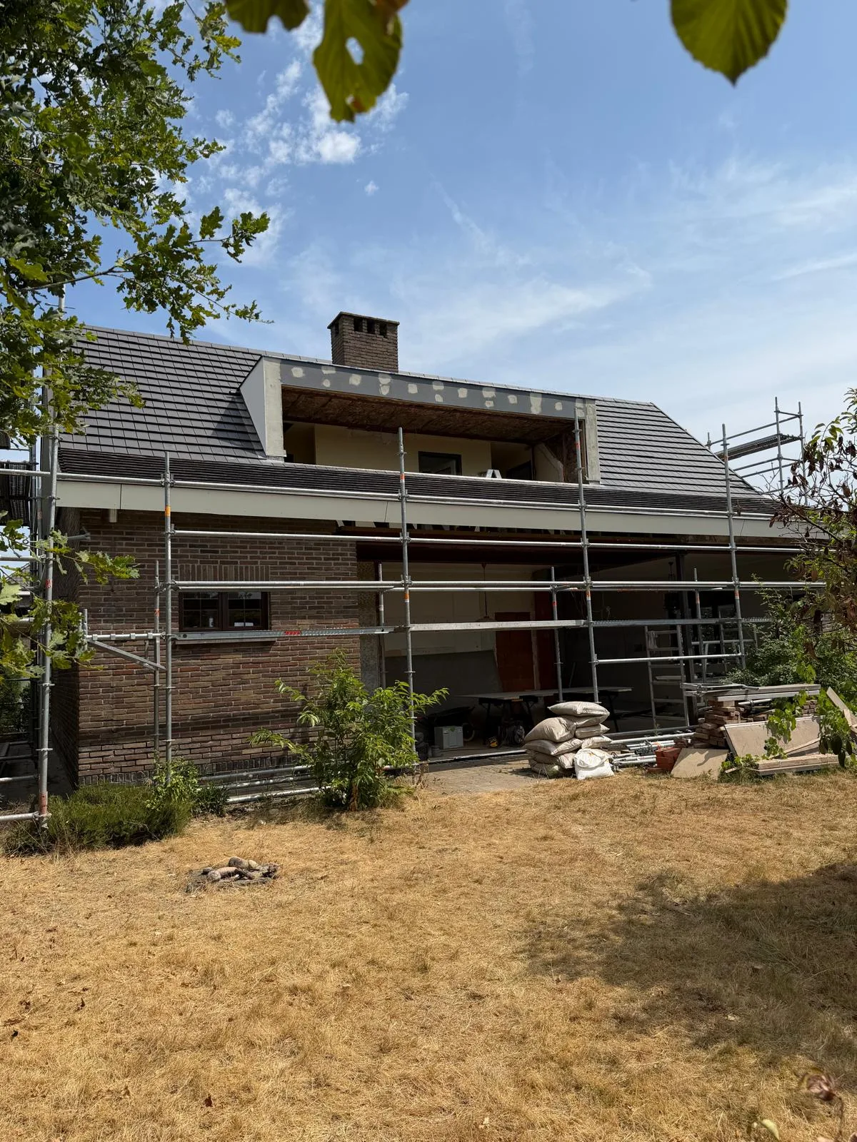Gevelrenovatie van een woning met steigers, metselwerk en dakbedekking in de opbouwfase