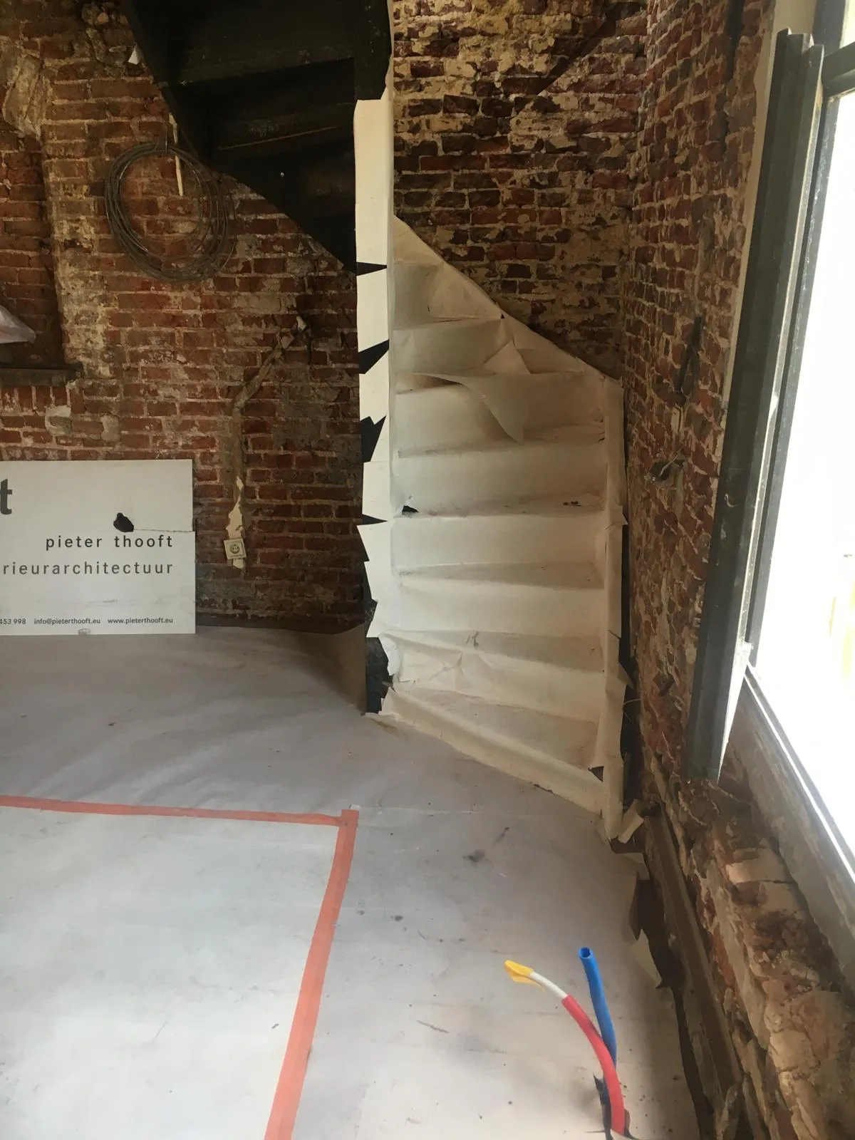 Trapopgang in renovatie met blootgelegde bakstenen muur en afplakband
