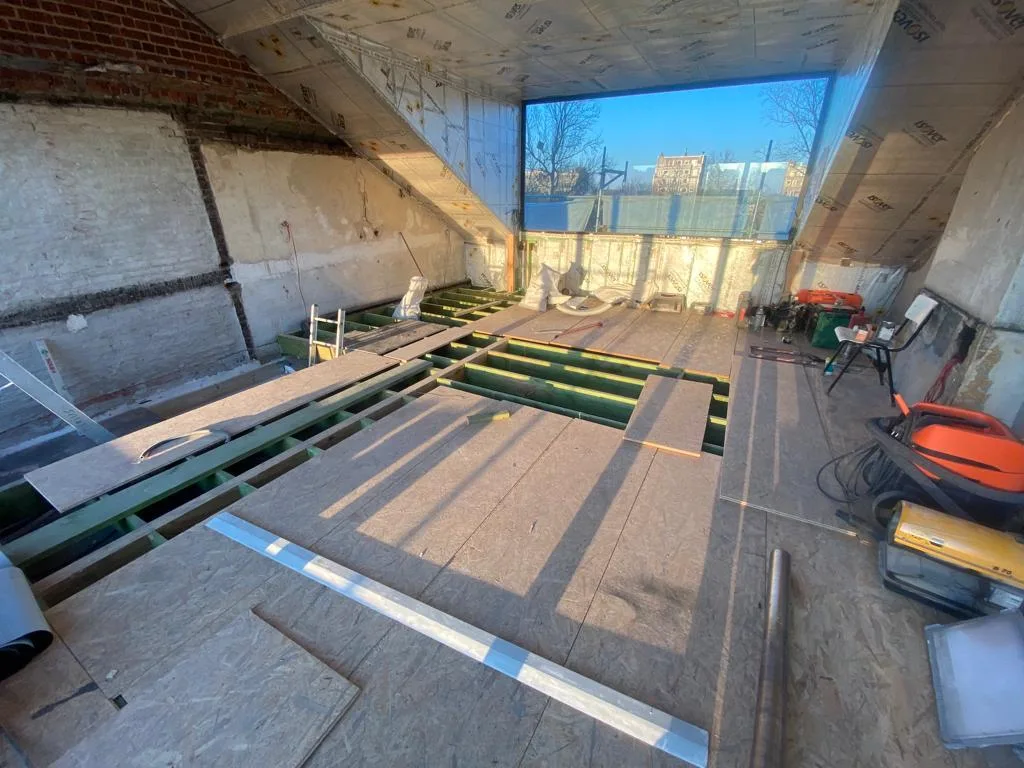 Binnenafwerking in aanbouw met houten balken en onafgebouwde vloer